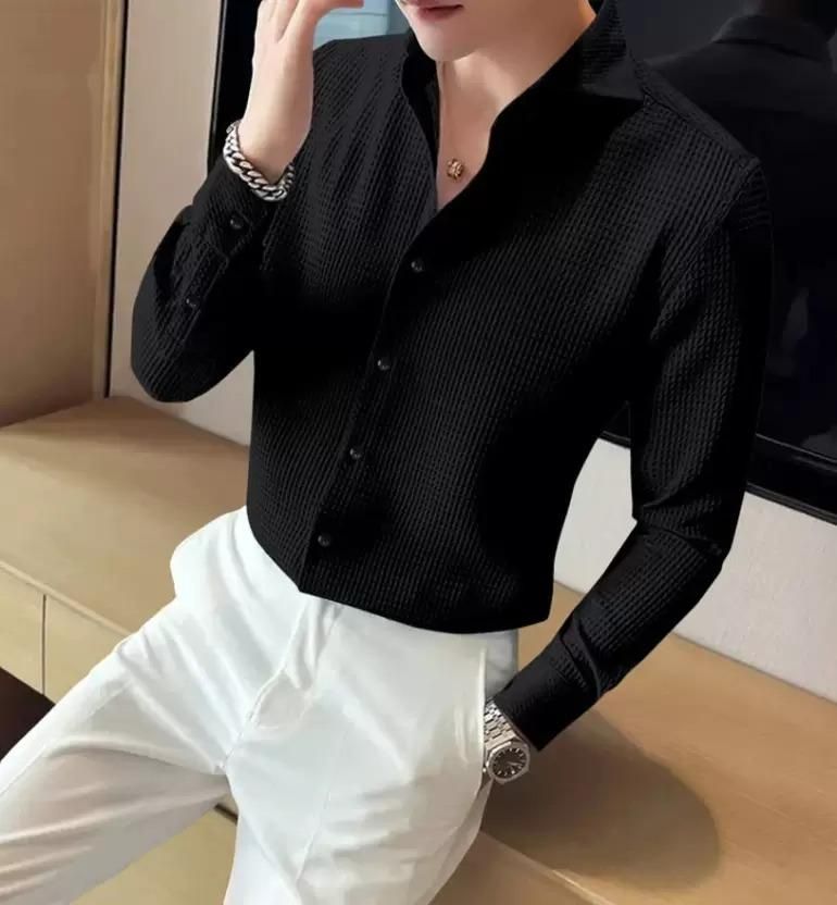 Person wearing a black textured shirt and white pants in an indoor setting.